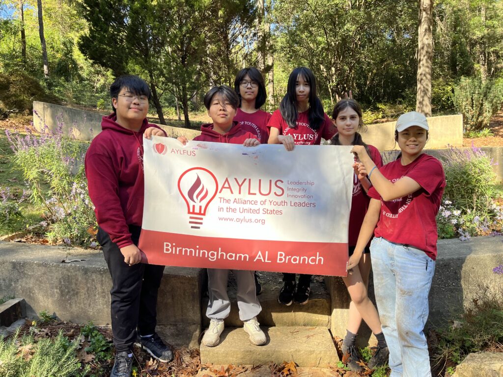 AYLUS members pose for a picture with the banner in front of the Little Ones Memory garden